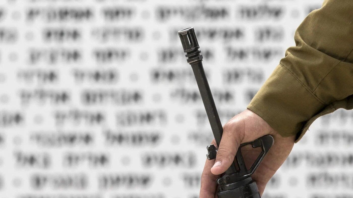 The gun of an Israeli soldier is seen in front of a commemorative plaque on 1 May 2017 (Jack Guez/AFP)